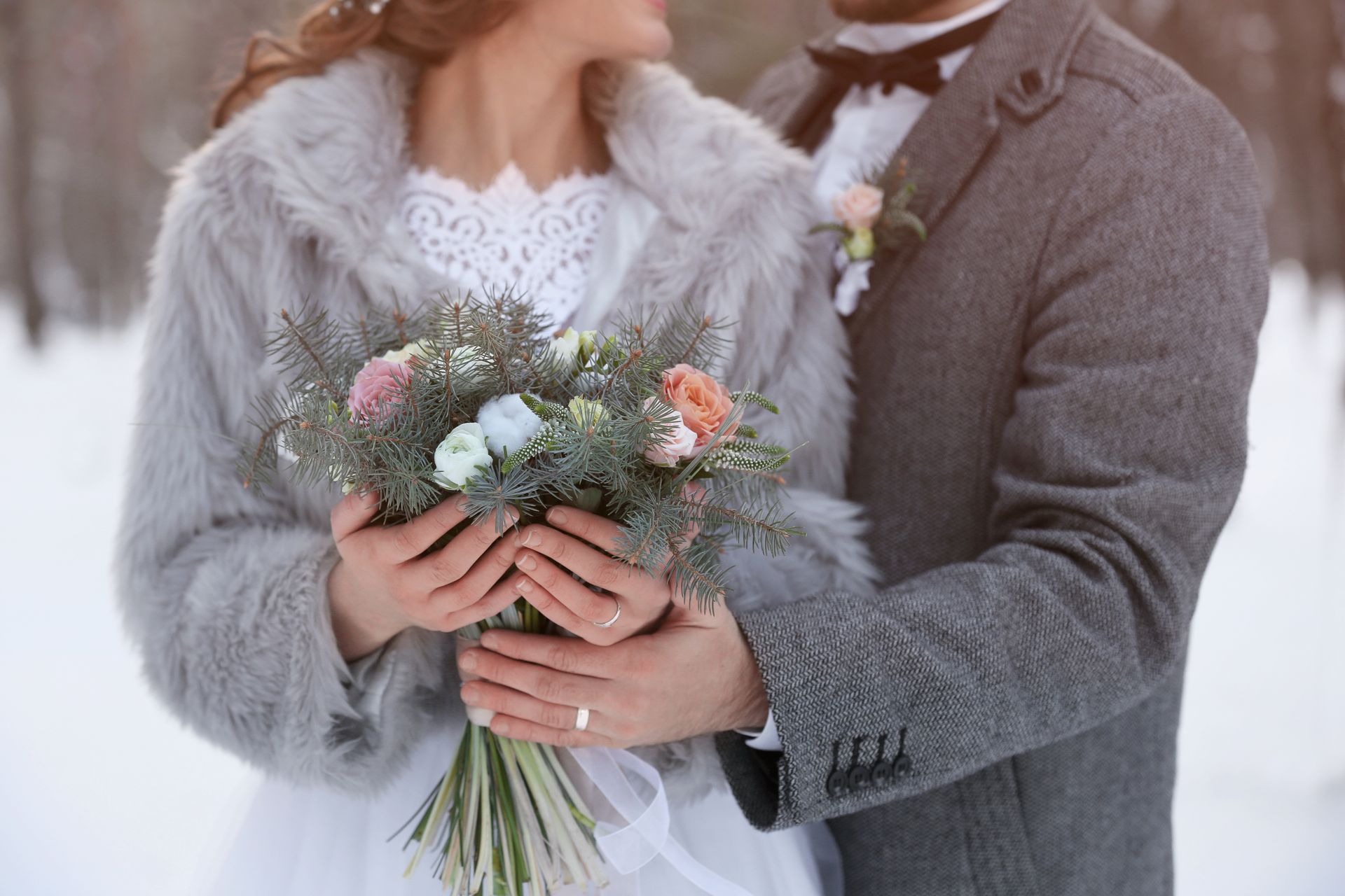 A bride and groom are standing in the snow holding a bouquet of flowers.
