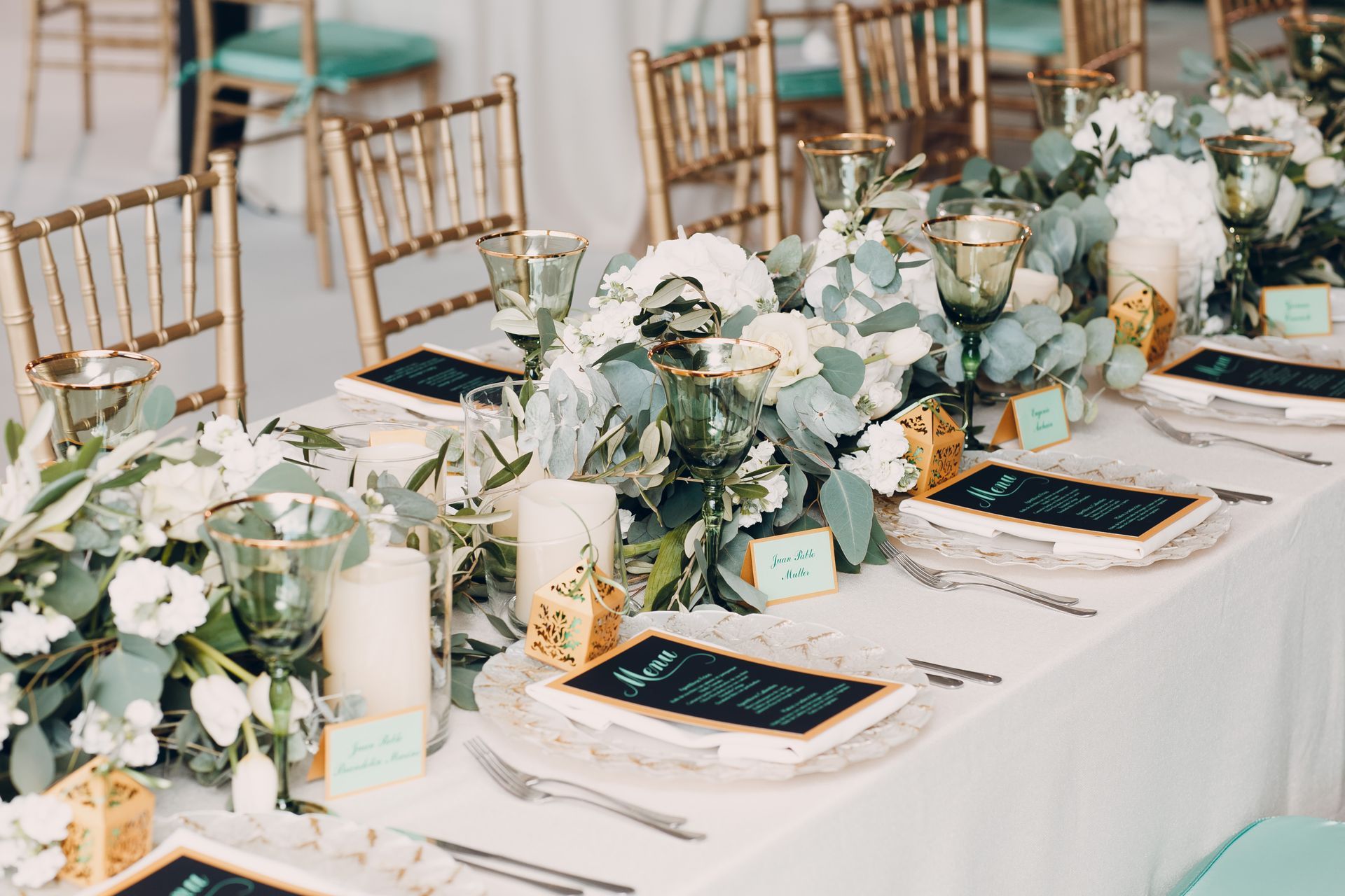 Formal wedding table setting with white and green floral arrangement, gold chairs, and place settings.