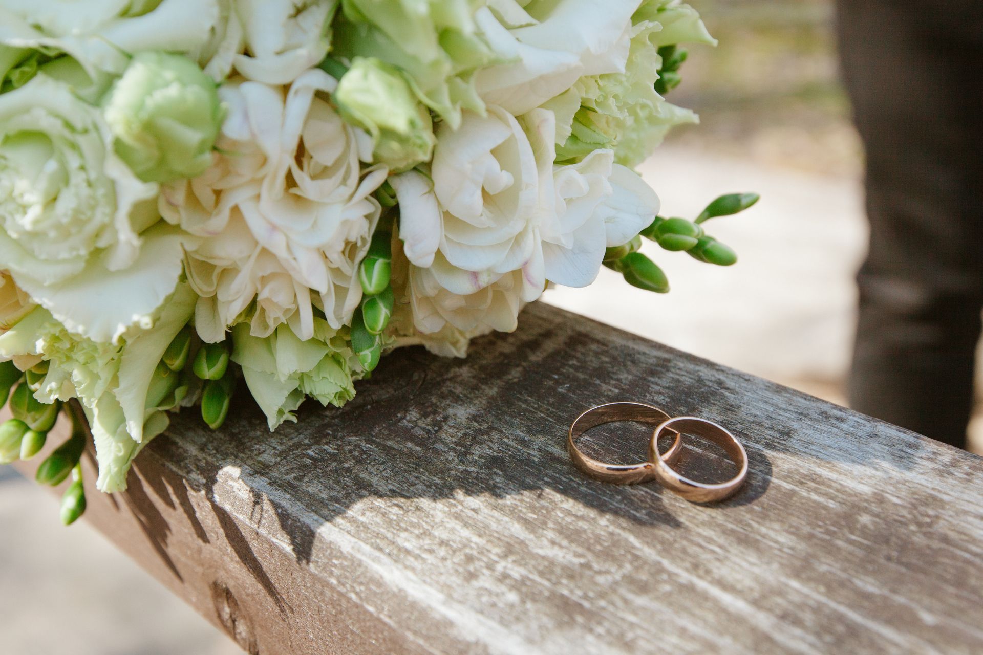 Two wedding rings are sitting on a wooden bench next to a bouquet of flowers.