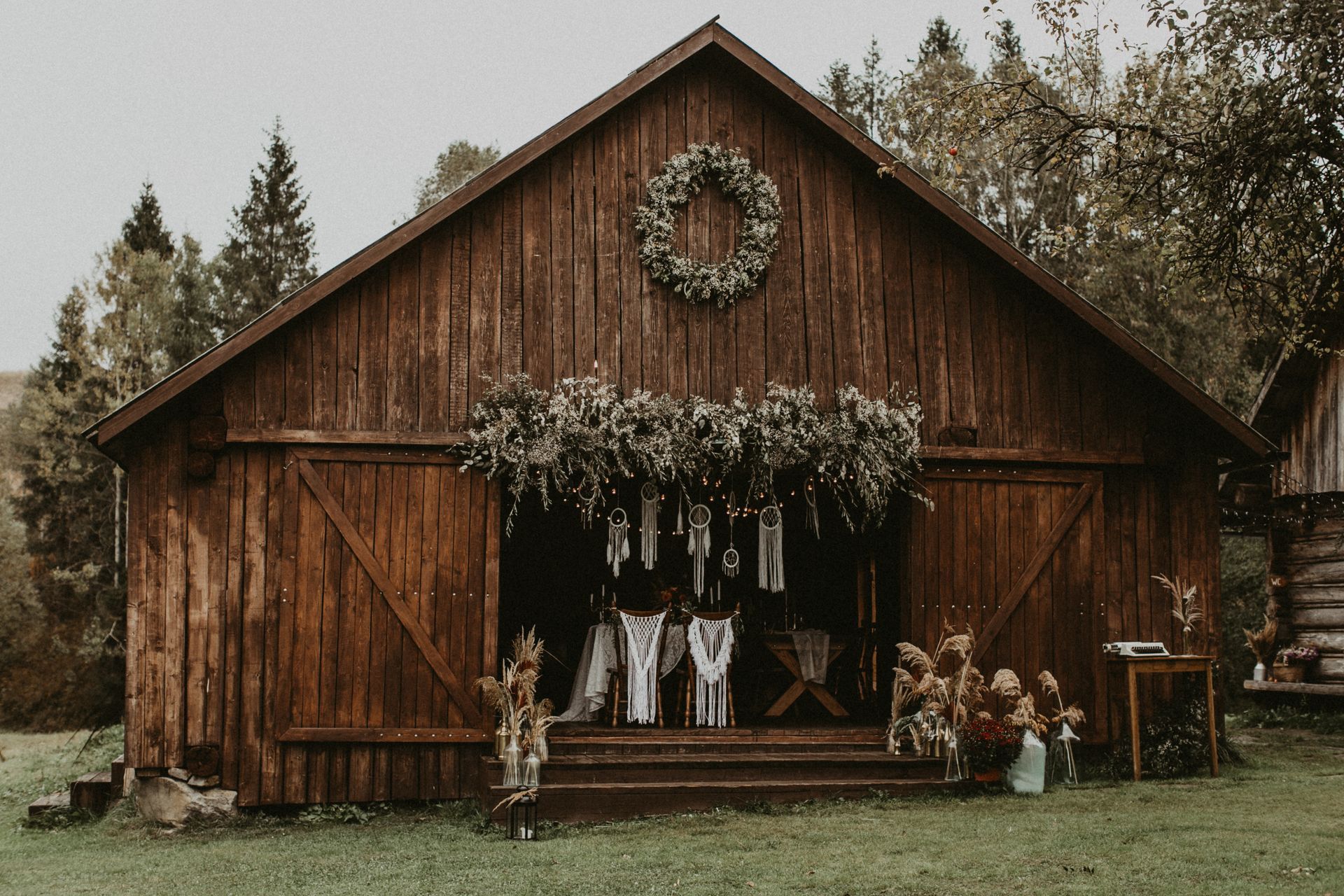 Wooden barn decorated with greenery, hosting an outdoor event with floral arrangements.