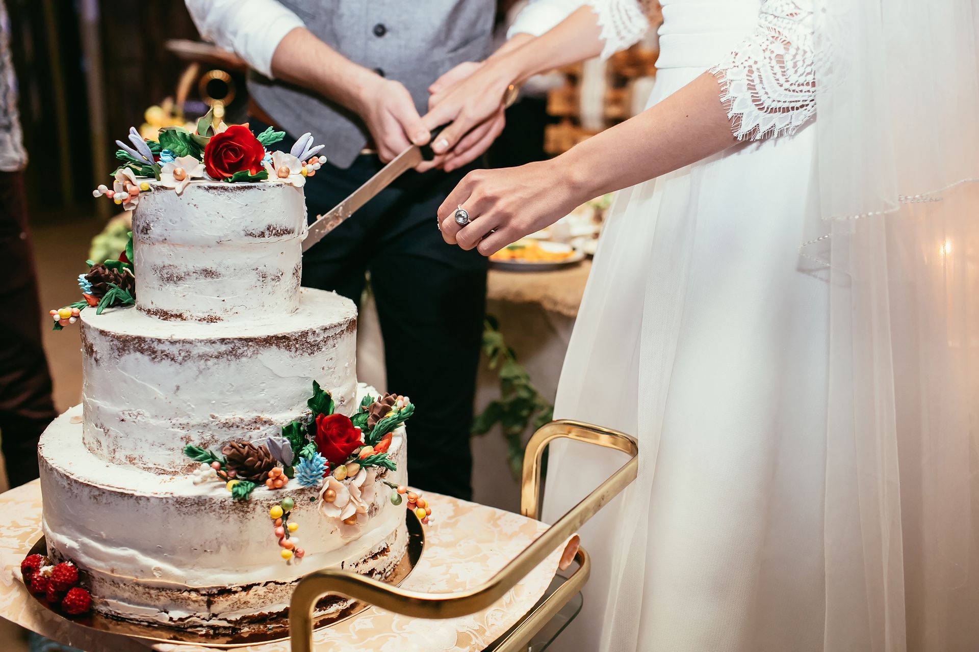 Bride and groom cutting a three-tiered wedding cake decorated with flowers.