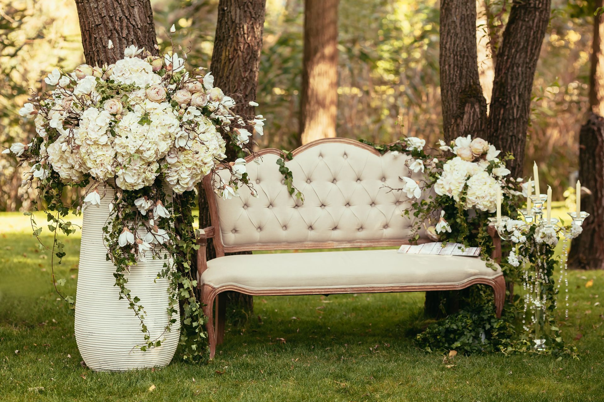 A decorative bench outdoors, surrounded by lush white flowers and greenery, in a sunny, grassy setting.