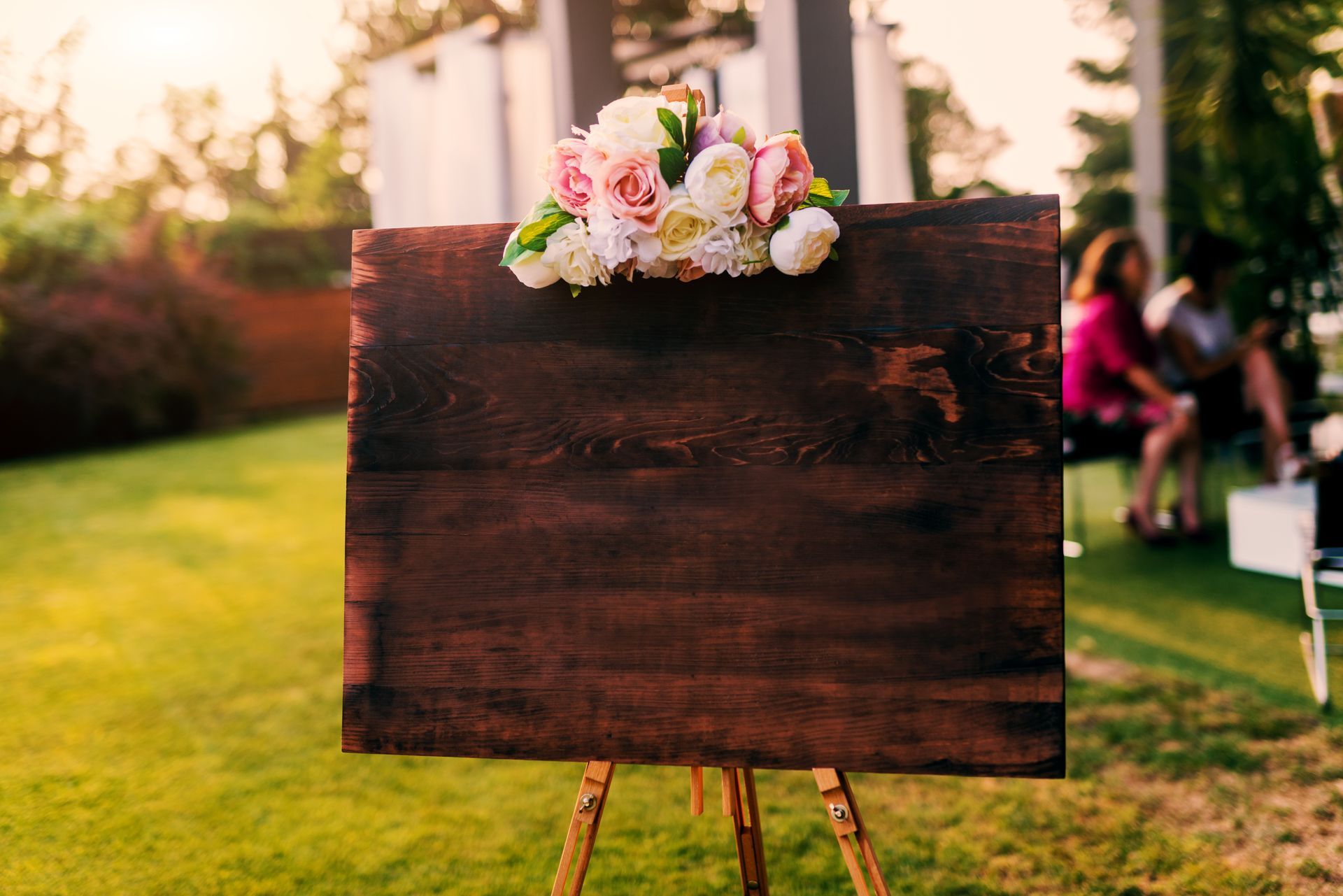 Wooden sign with flowers on easel outdoors, ready for a message.