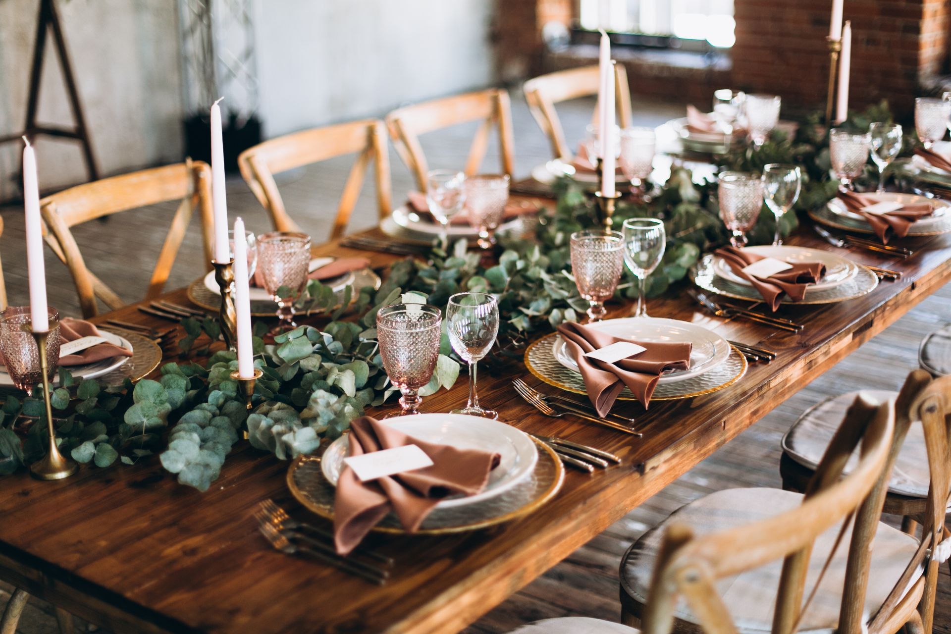 Rustic wedding reception table setting with greenery, candles, and place settings.