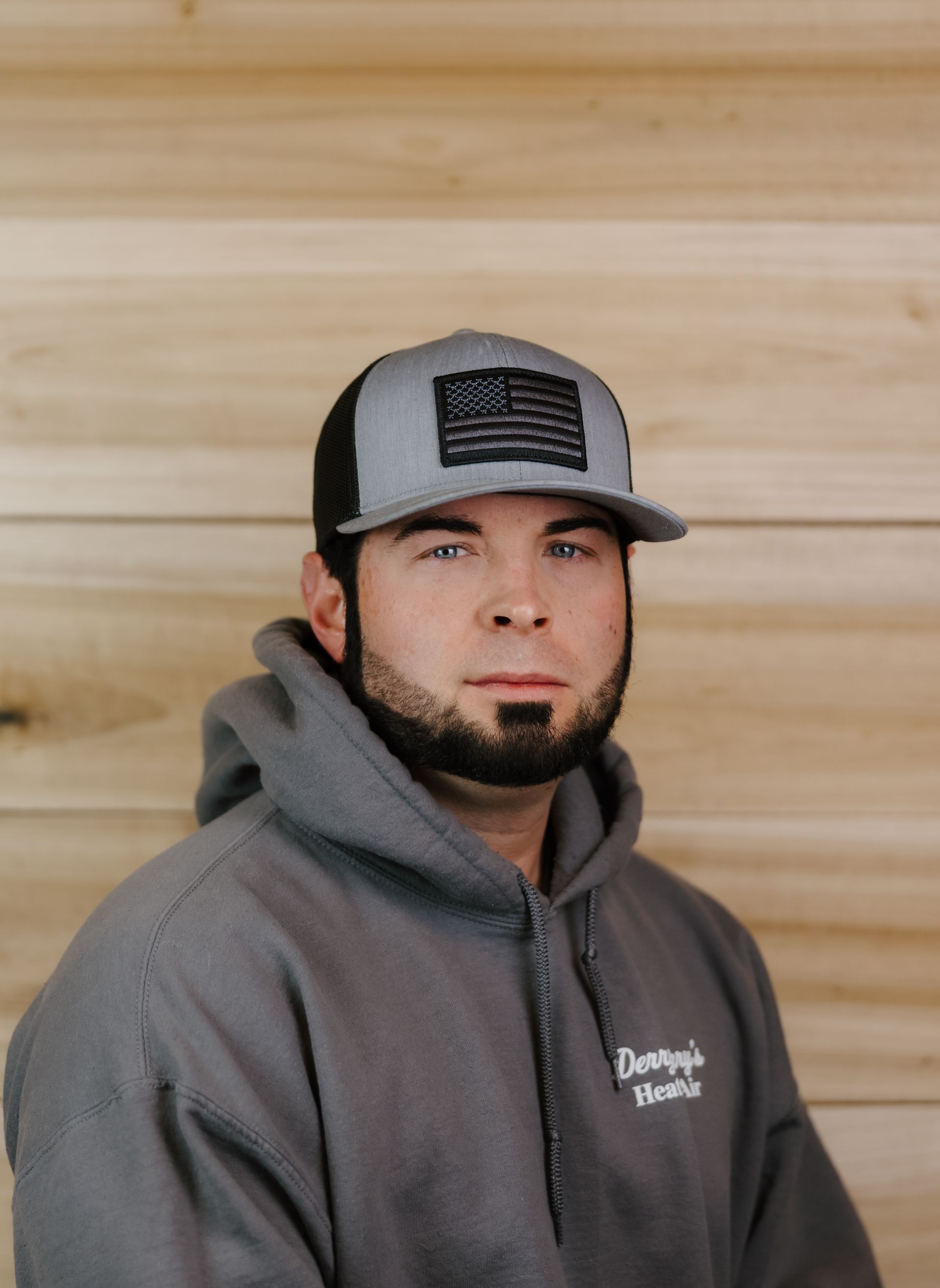 Man in grey hoodie and hat with American flag patch.
