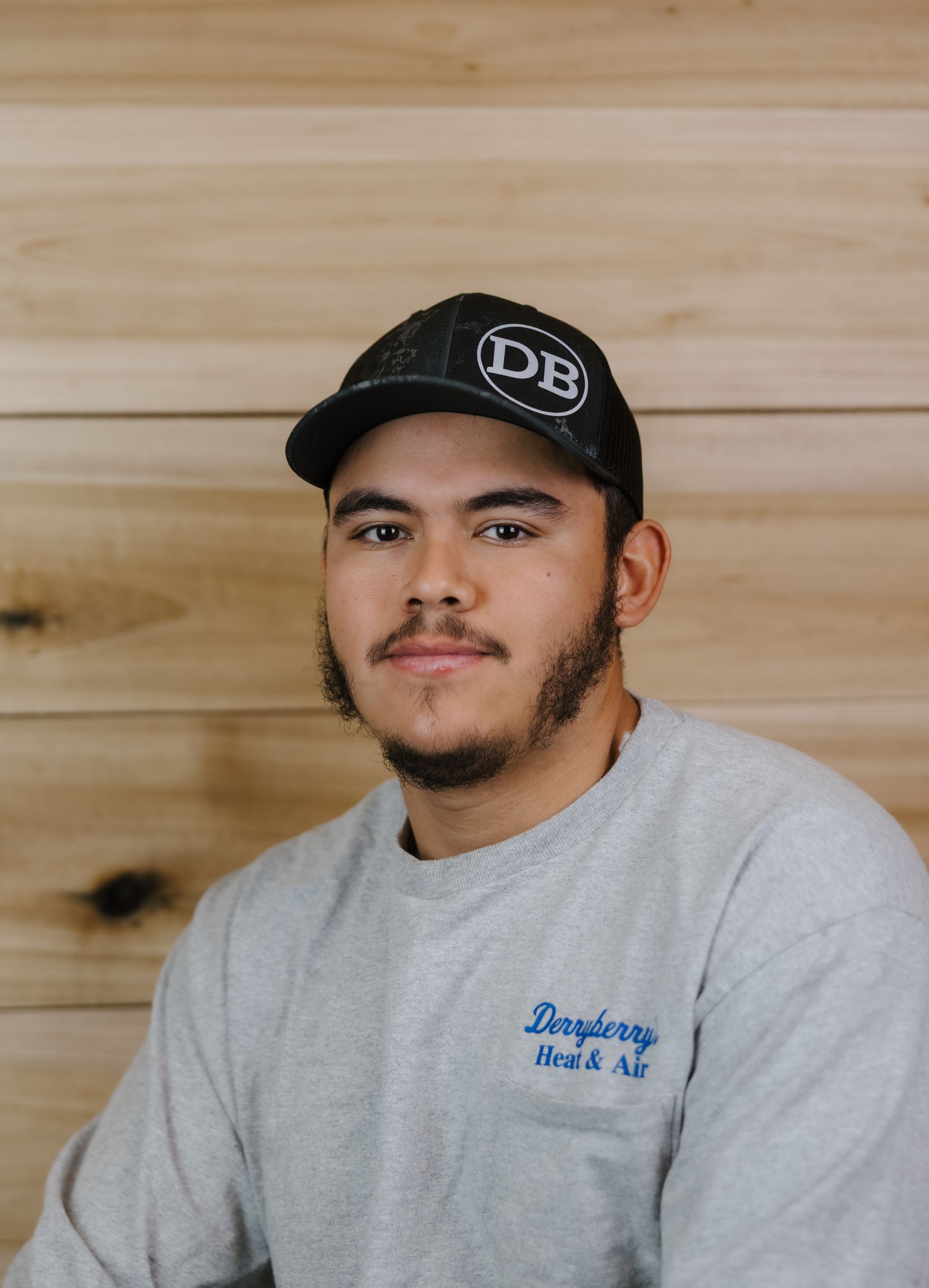 Man wearing a cap and sweatshirt, standing in front of a wood background.