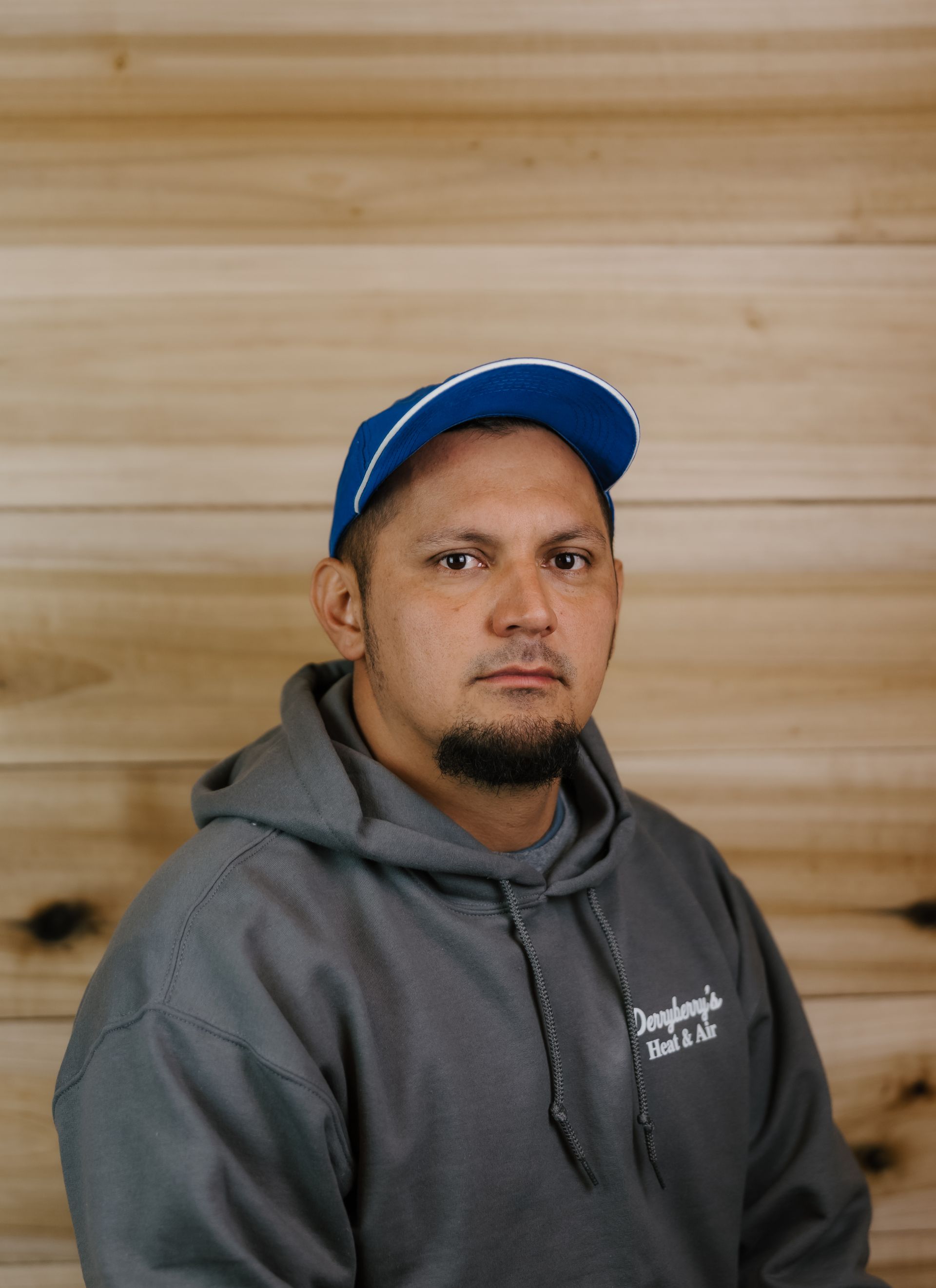 Man in a blue cap and grey hoodie, standing in front of a wood background.