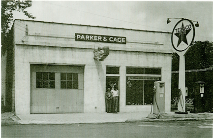 A black and white photo of a gas station named Parker & Cage, with a Texaco sign. Two people stand in the doorway.
