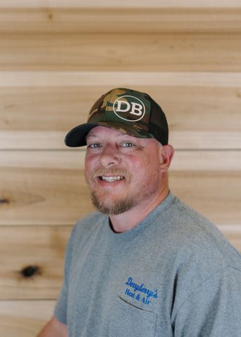 Man wearing a gray beanie and hooded sweatshirt against a wood-paneled wall, looking at the camera.