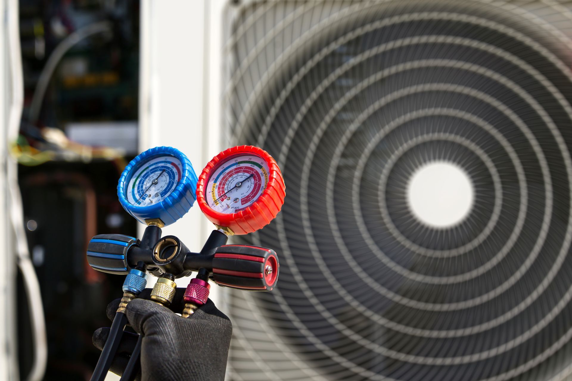 HVAC gauges connected to an outdoor unit, blue and red dials, black gloved hand.