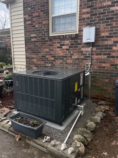 Central air conditioning unit outside brick building. Black unit with small drain pipe and electrical box.