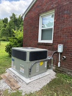 Air conditioning unit on a gravel pad next to a red brick building with a window.