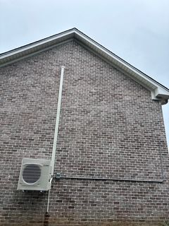 Air conditioning unit mounted on a brick wall with white conduit running up to the roof.