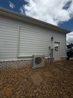 White building with an AC unit, gravel, and door. Blue sky with clouds overhead.