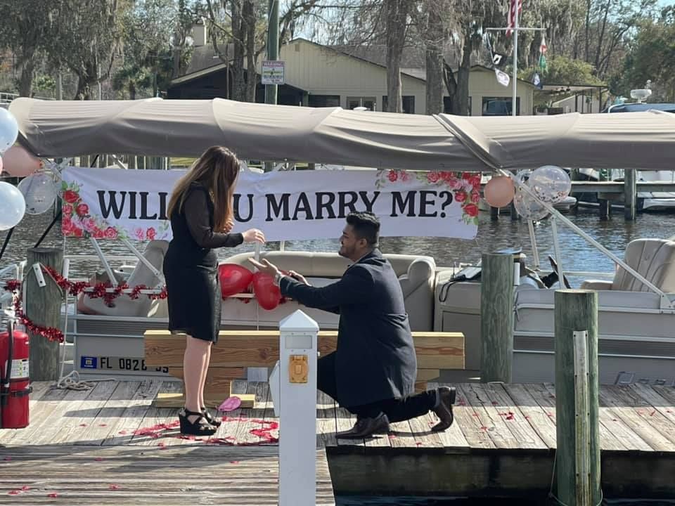A man is kneeling down in front of a sign that says will you marry me.