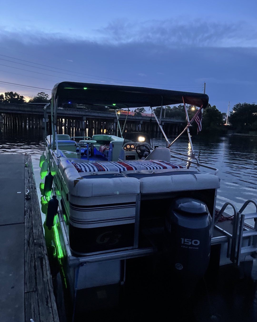 A pontoon boat is docked at a dock at night.