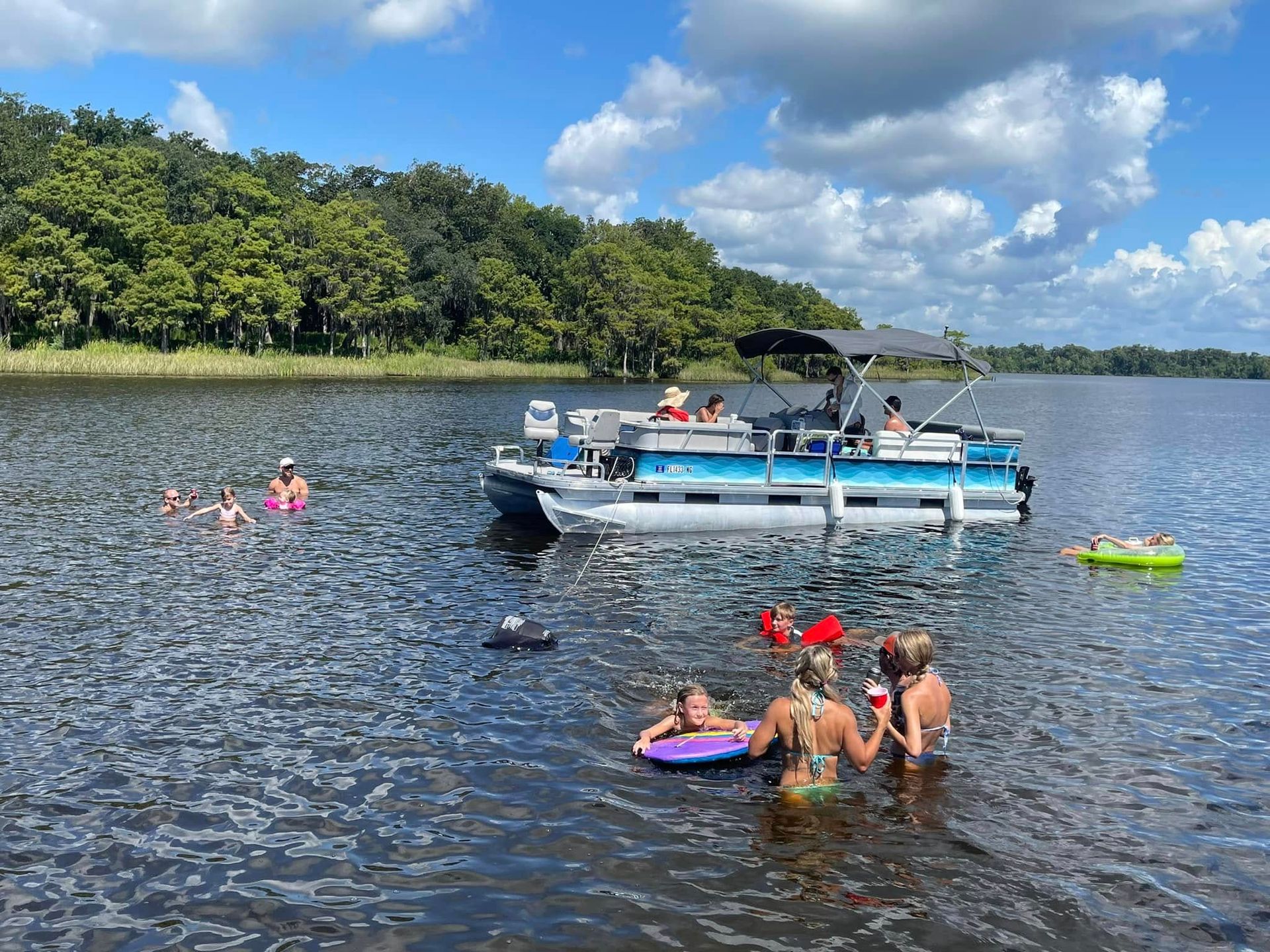 A group of people are swimming in a lake next to a pontoon boat.