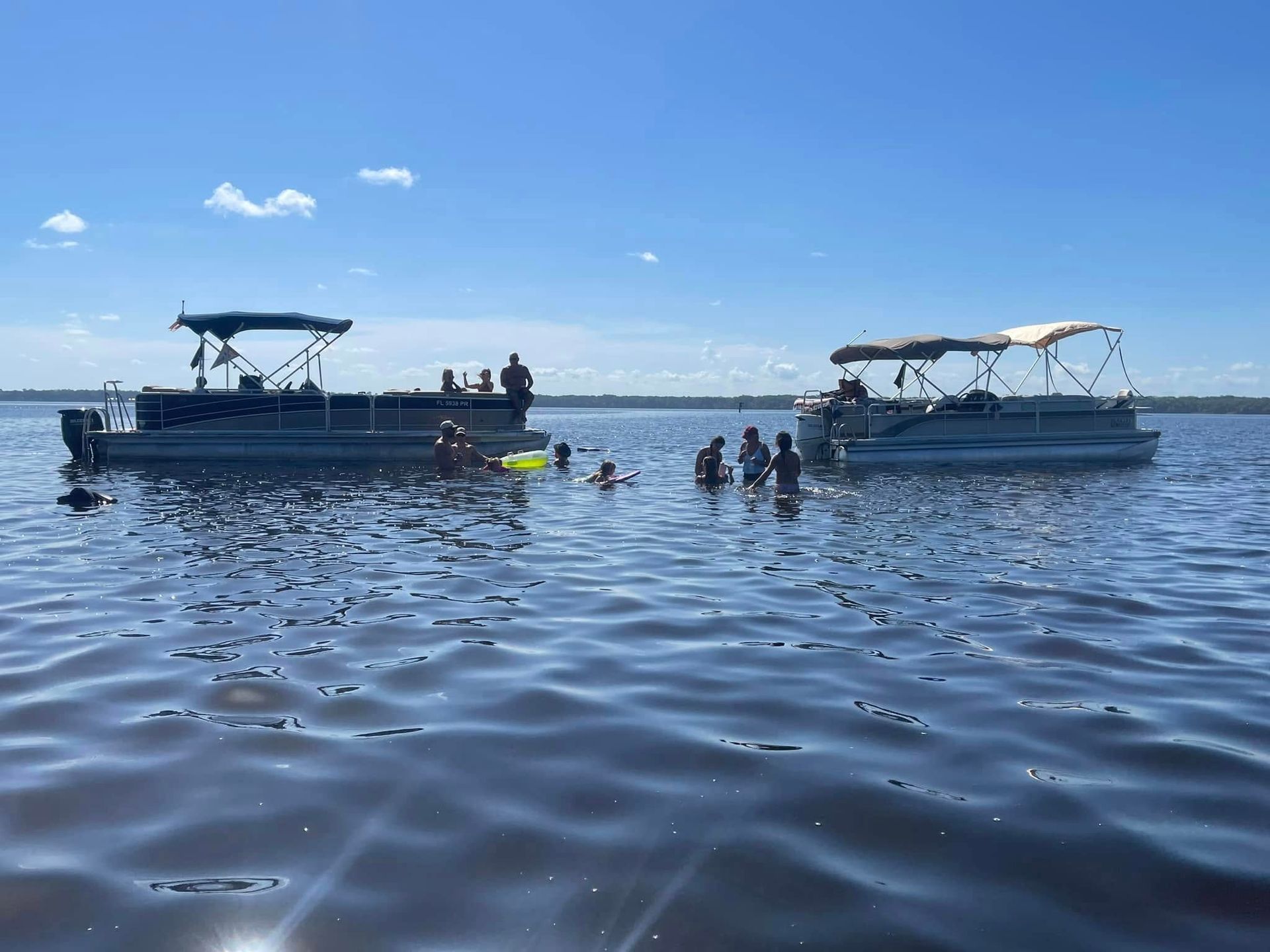 A group of people are swimming in a lake next to two pontoon boats.