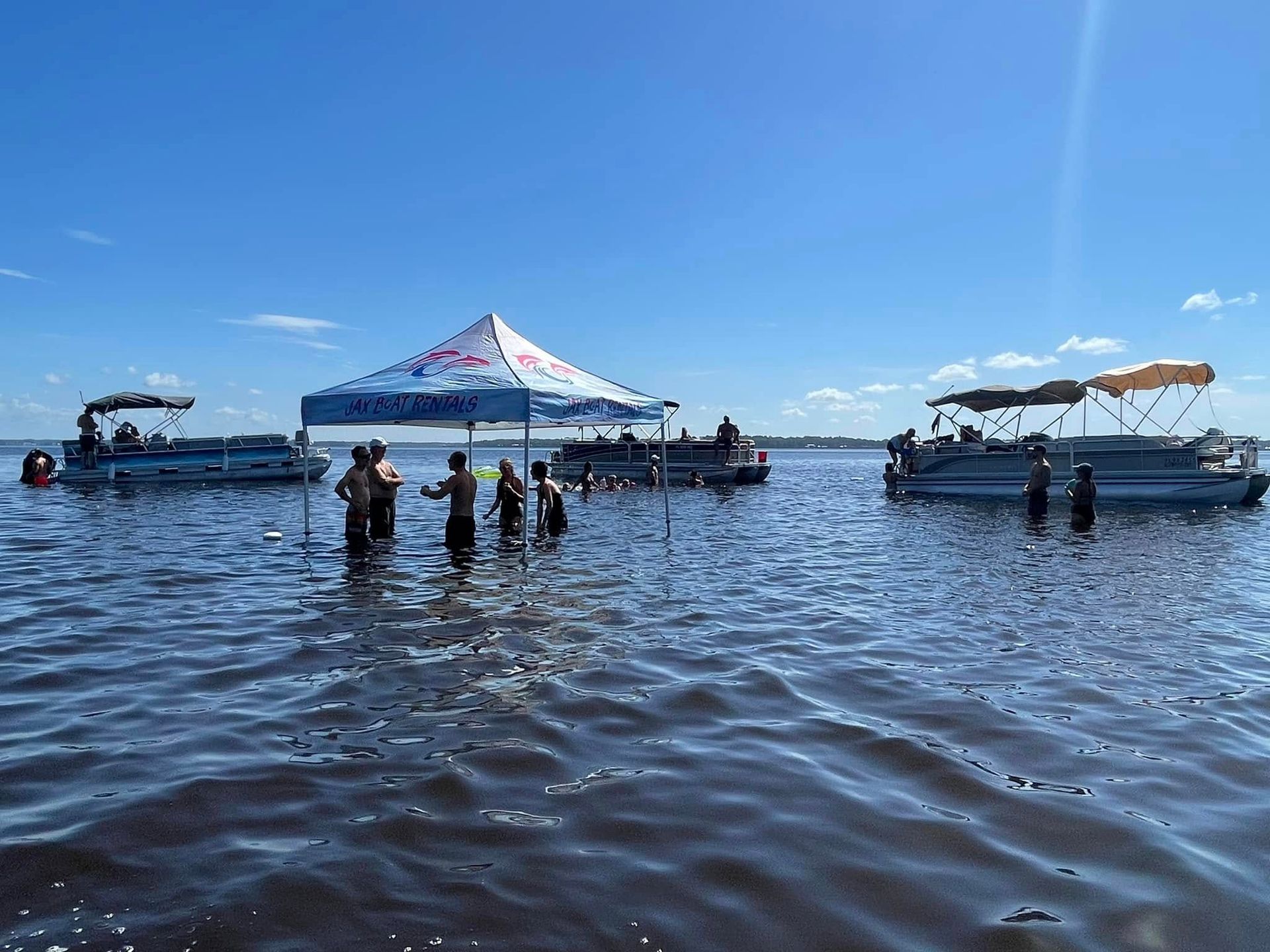 A group of people are standing in the water next to boats.