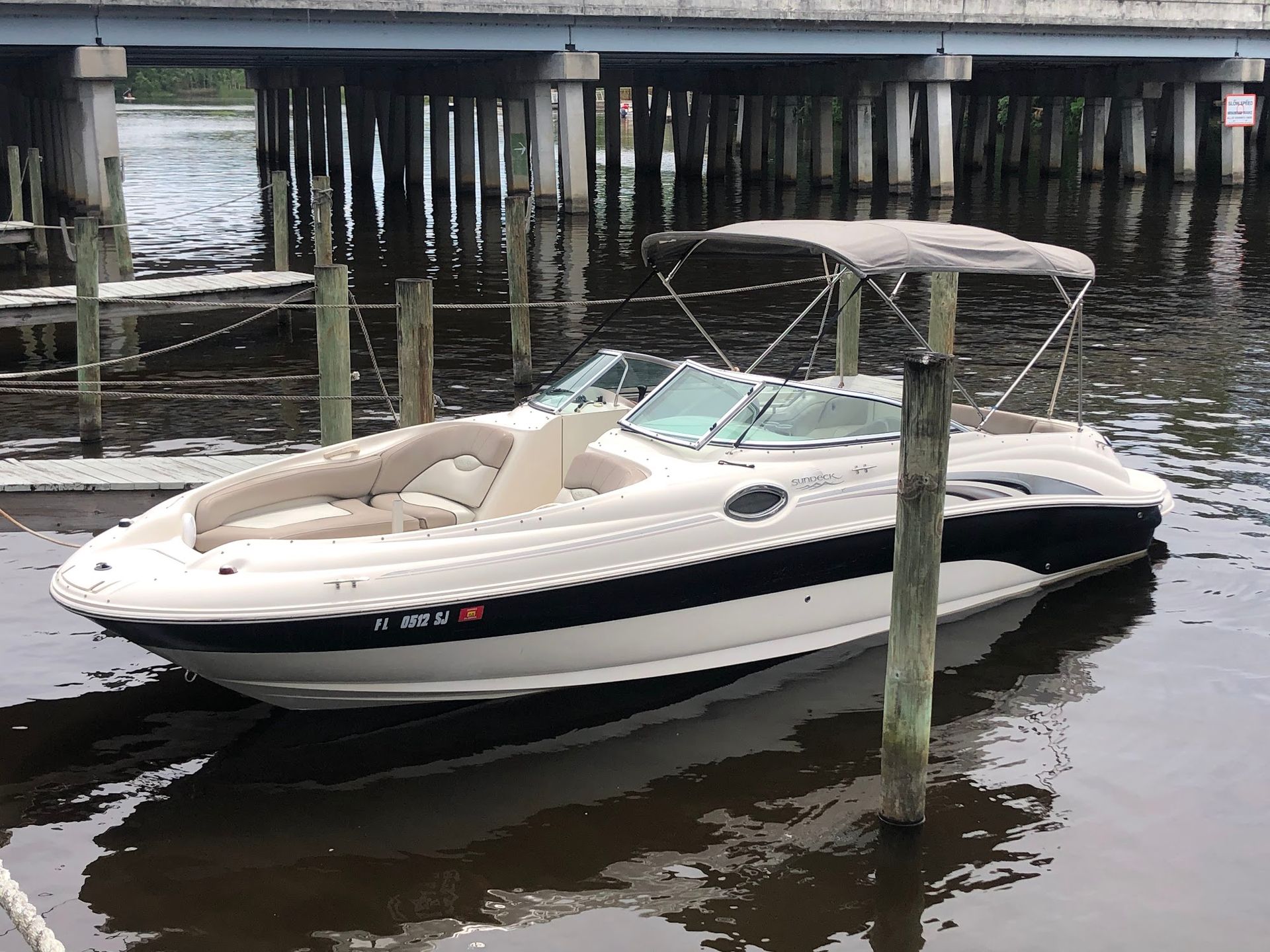 A white boat with a canopy is docked under a bridge in the water.