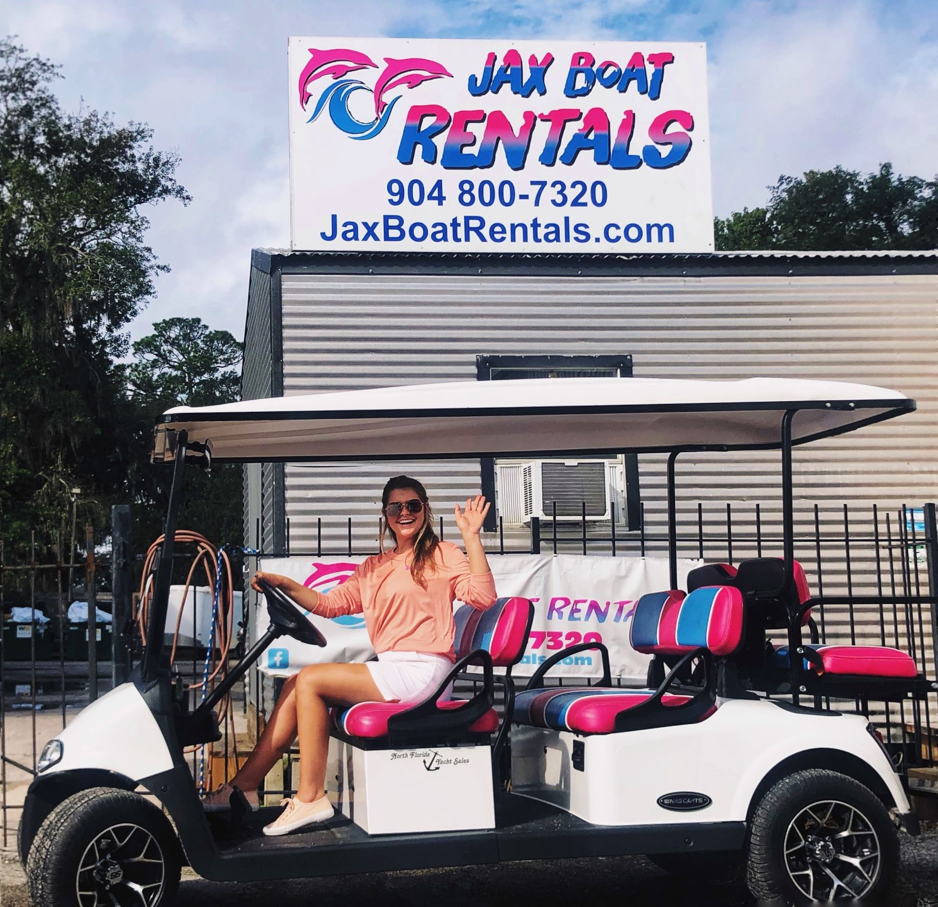 A woman is sitting in a golf cart in front of a jax boat rentals sign