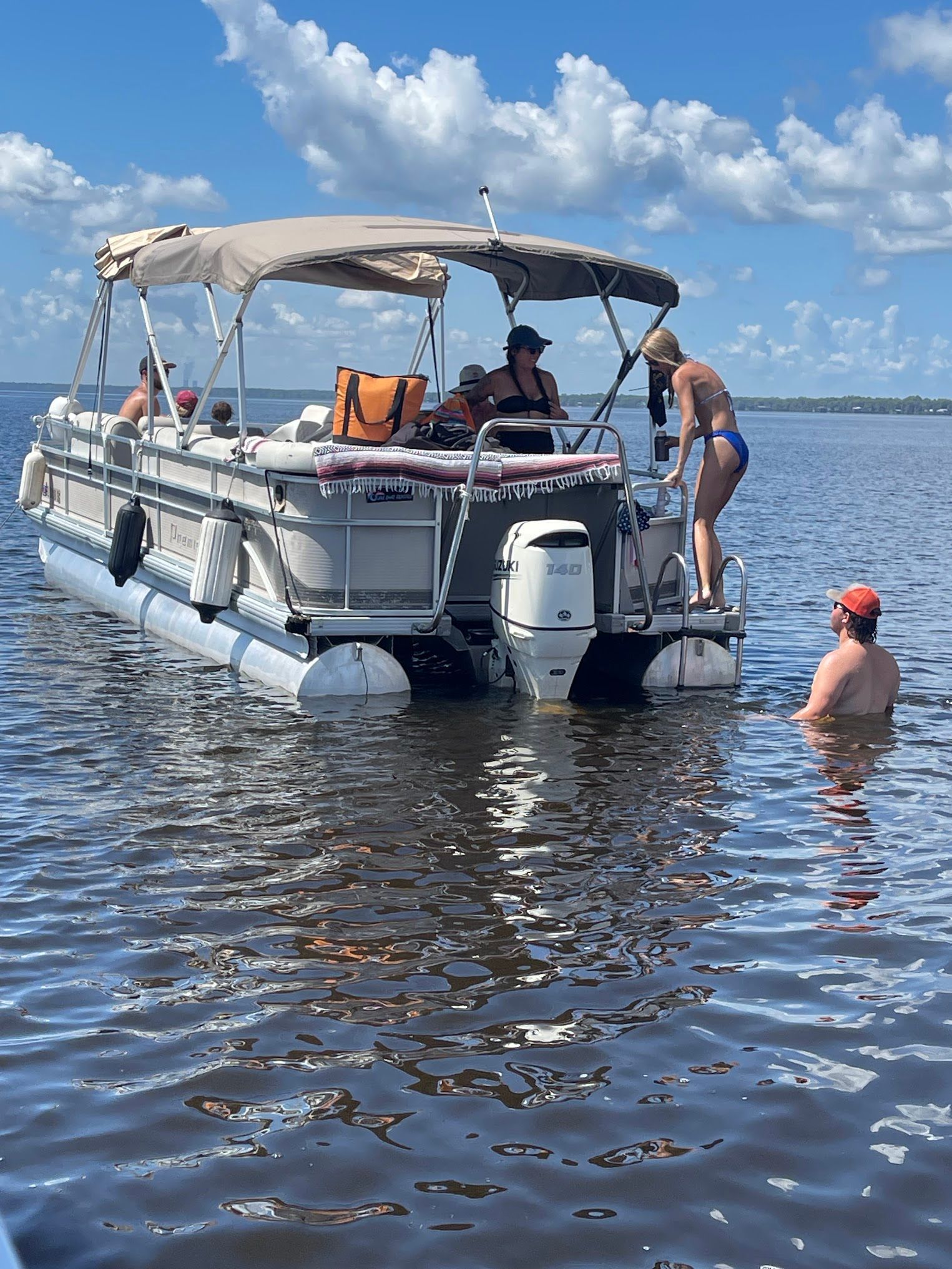 A pontoon boat with people on it is floating on top of a body of water.