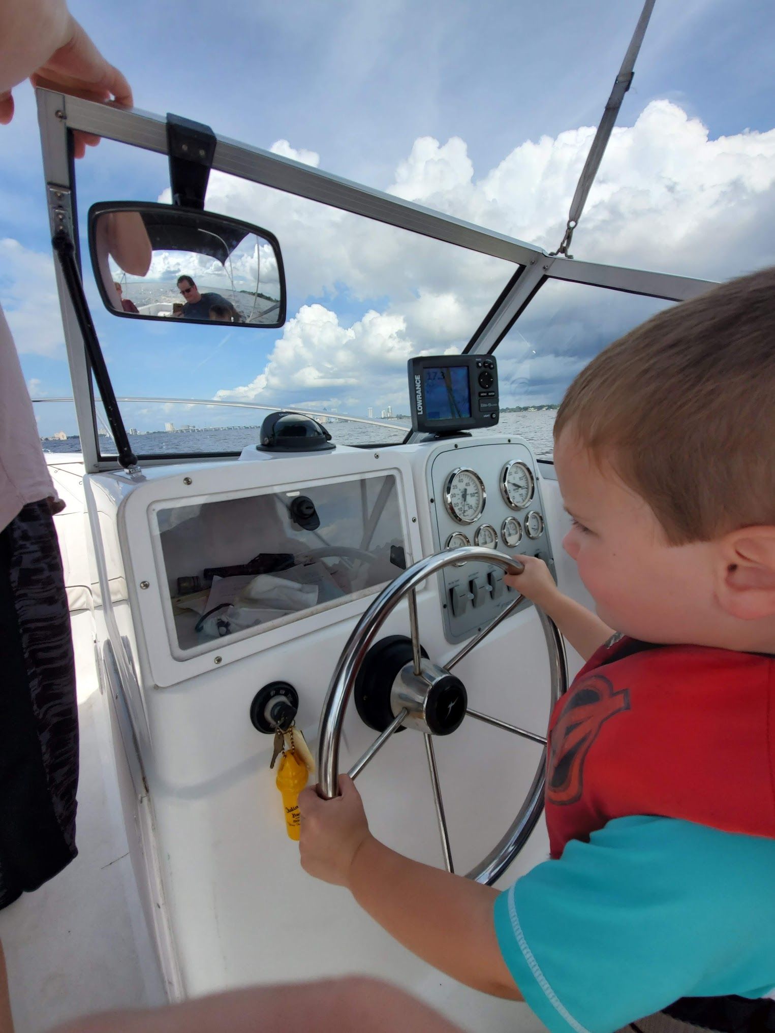 A little boy is sitting at the steering wheel of a boat