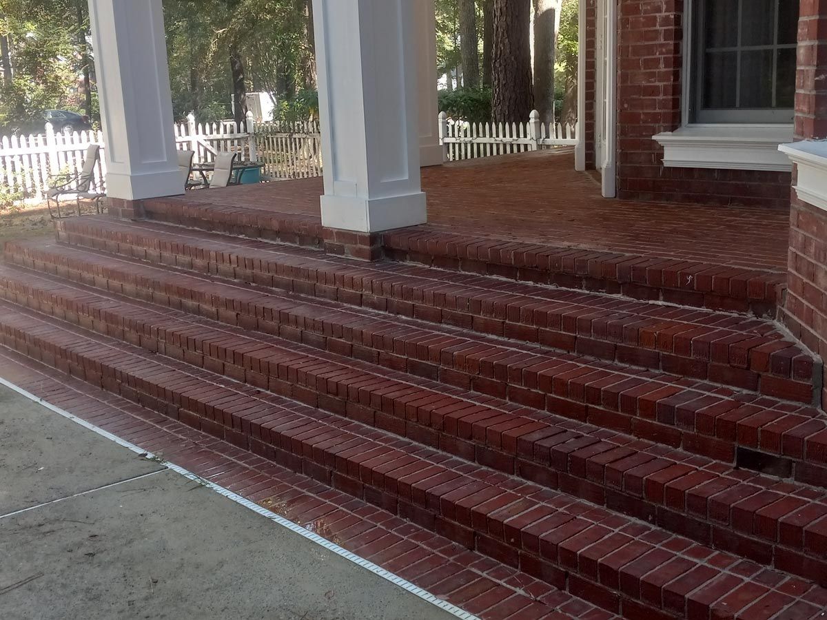 A brick porch with stairs leading up to it and a white picket fence.
