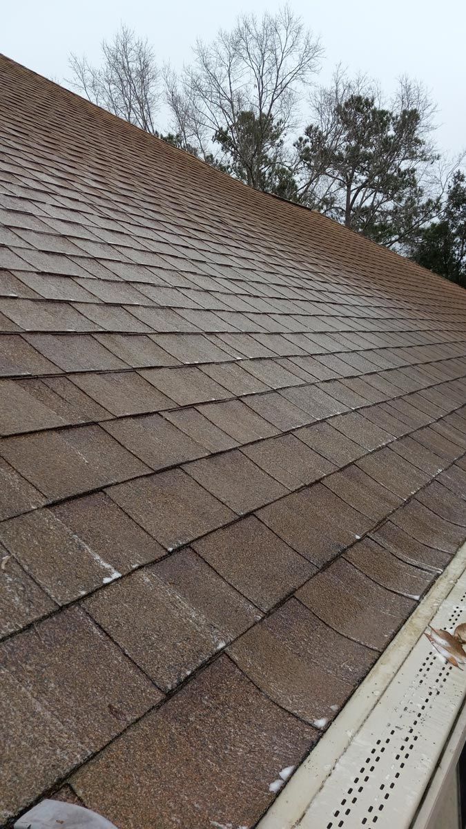 A close up of a roof with a gutter and trees in the background.