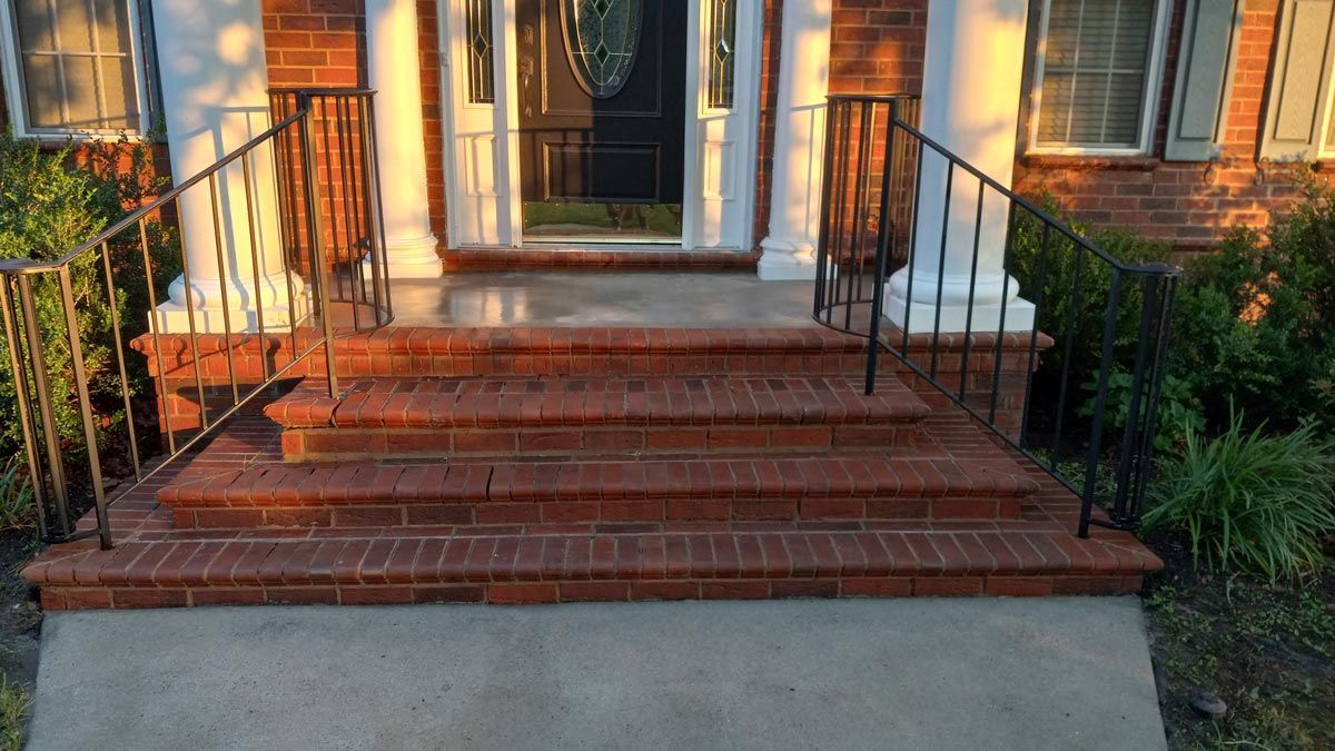 The front steps of a brick house with a wrought iron railing.