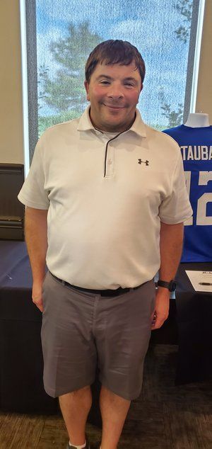 A man in a white shirt and shorts is standing in front of a table.