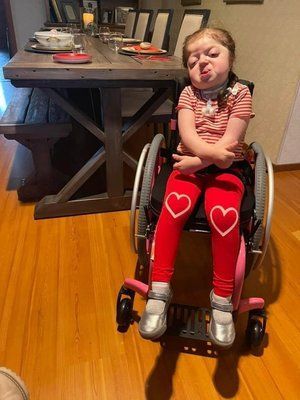 A little girl in a wheelchair is making a funny face.