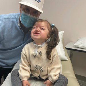 A man wearing a hat and a mask is sitting next to a little girl.