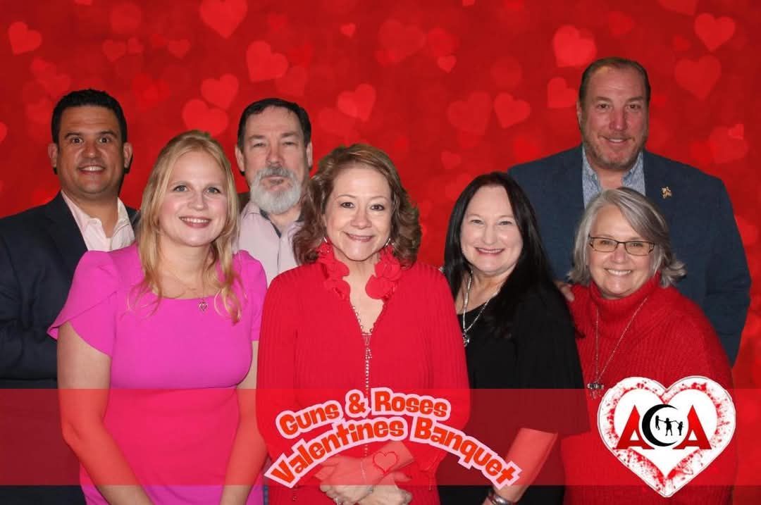A group of people are posing for a picture in front of a red background with hearts.