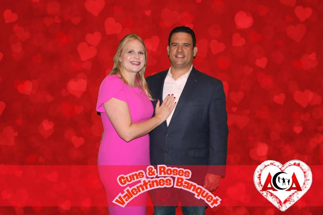 A man and a woman are posing for a picture in front of a red background with hearts.