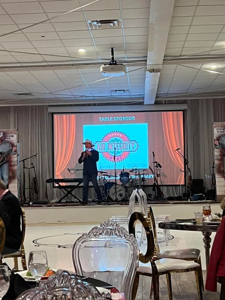 A man is singing into a microphone on a stage in front of a large screen.