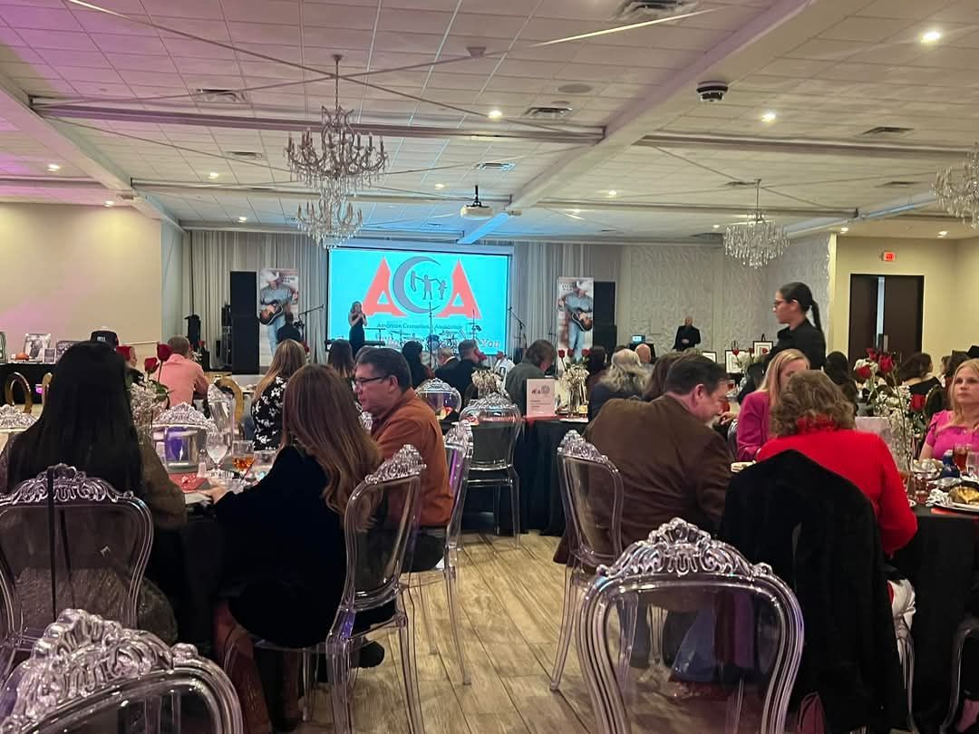 A large room filled with people sitting at tables in front of a large screen.