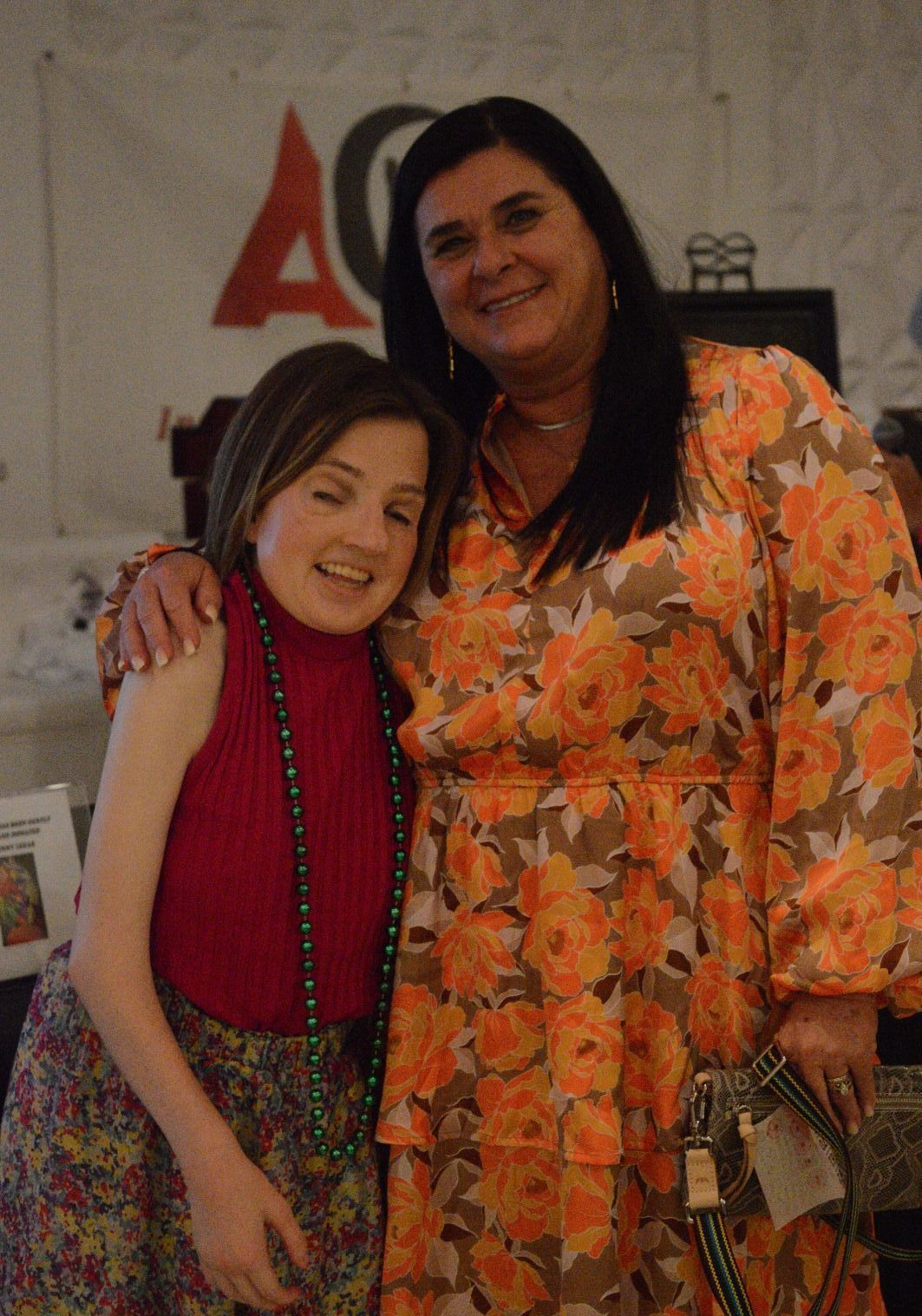 Two women are posing for a picture together in front of a wall with the letter a on it.