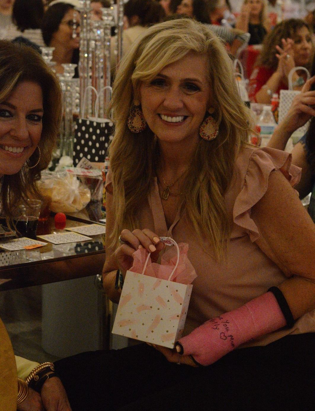 Two women are sitting at a table and one is holding a pink gift bag