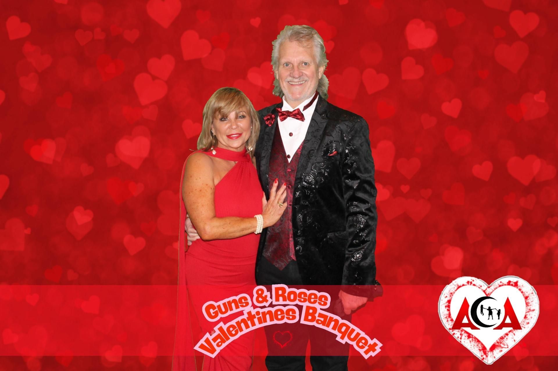 A man and a woman are posing for a picture in front of a red background with hearts.