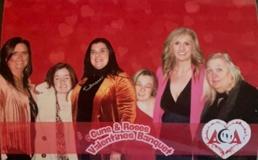 A group of women are posing for a picture in front of a red background that says valentines banquet