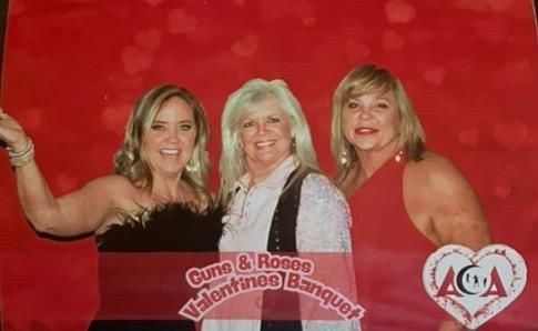 Three women are posing for a picture in front of a red background.