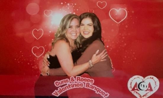 Two women are hugging each other in front of a red background with hearts.