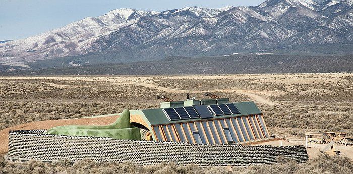 A house in the middle of a desert with mountains in the background.