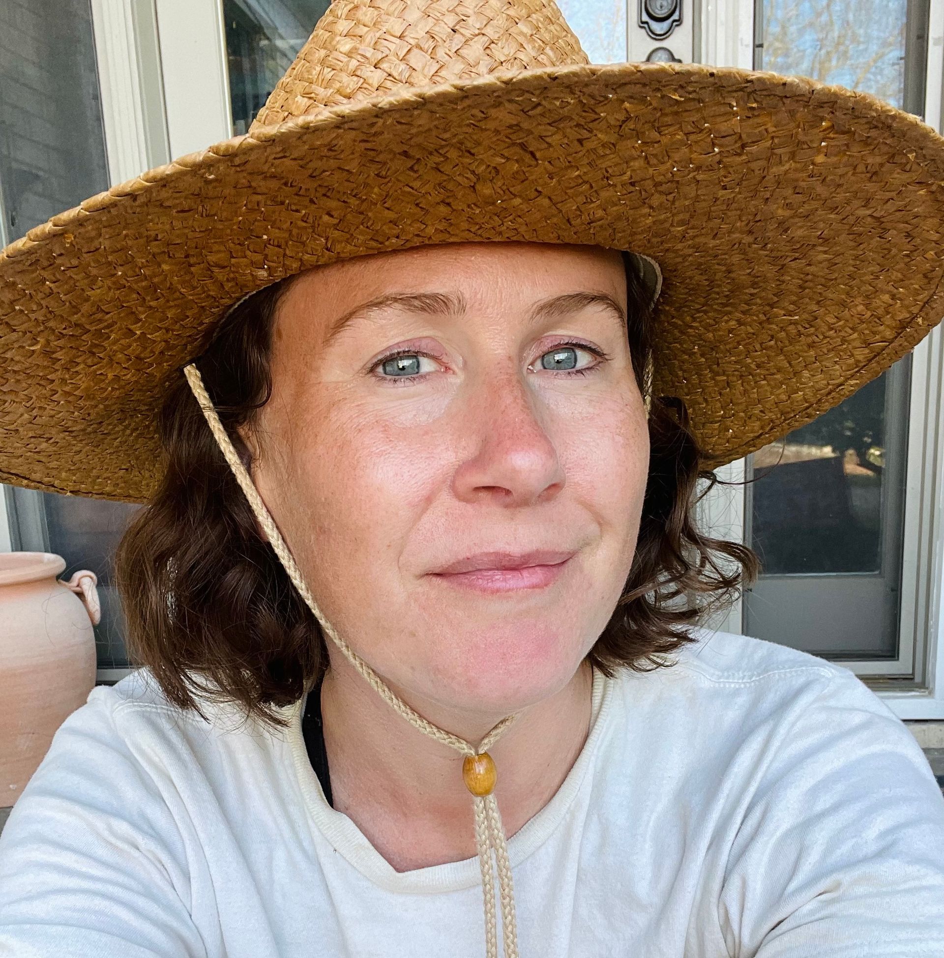 Woman wearing a straw hat, smiling, outdoors.