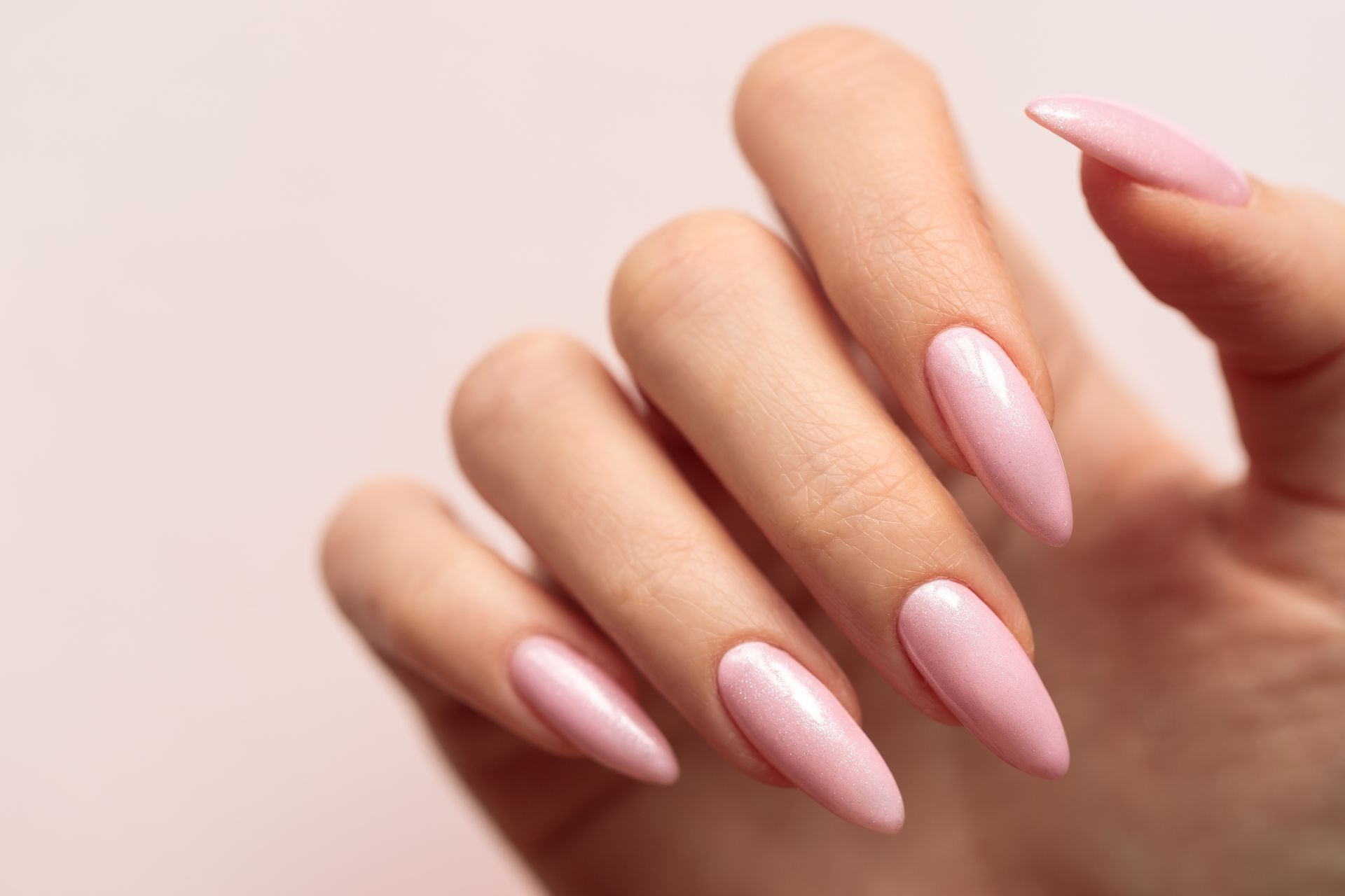 Eine Nahaufnahme der Hand einer Frau mit langen rosa Nägeln.