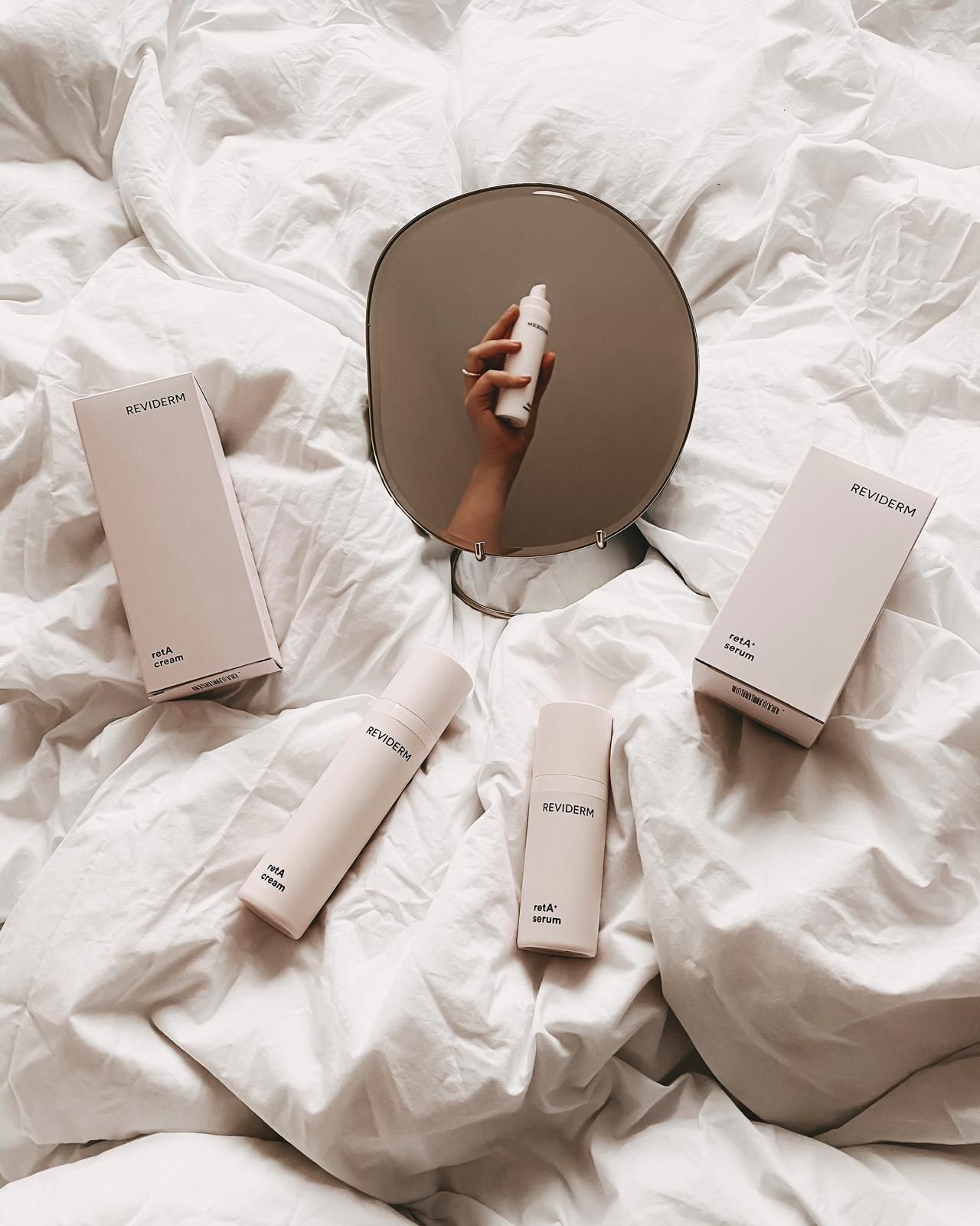 Eine Person hält eine Flasche Lotion vor einem Spiegel auf einem Bett.