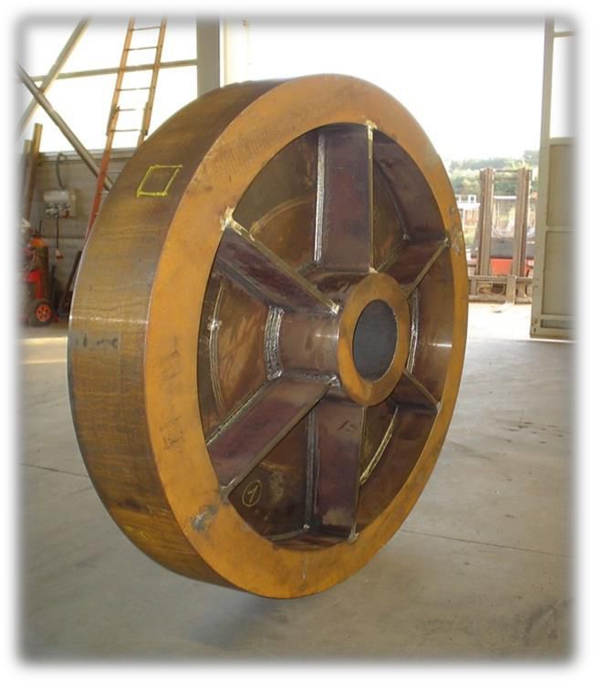 Grande ruota industriale color bronzo, probabilmente per macchinari, per interni. Presenta un mozzo centrale con raggi radiali.