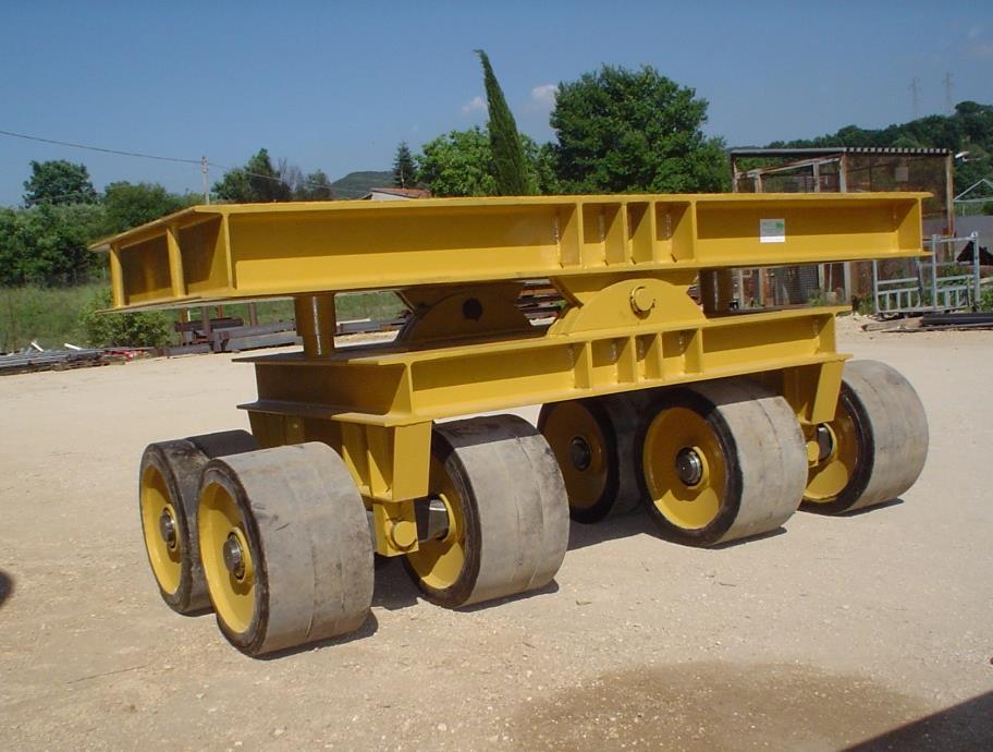 Un carrello da rimorchio industriale giallo per carichi pesanti, dotato di otto ruote in gomma, posizionato su una superficie ghiaiosa all'aperto.