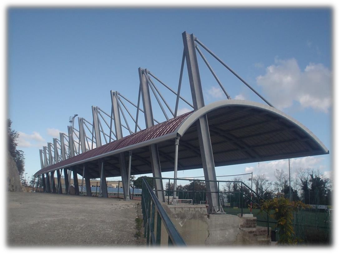 Una moderna struttura curva in metallo, sostenuta da pilastri in acciaio angolati e cavi di tensione, che si staglia contro un cielo blu.